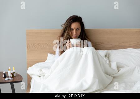 Unglückliche Frau, die eine Tasse Tee hält und im Bett sitzt Stockfoto