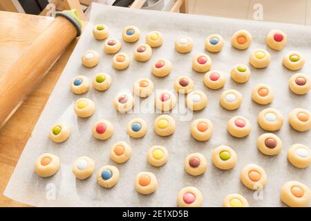 Nahaufnahme einer Menge von Cookies mit verschiedenen farbigen Schokoladenstückchen auf einem Backpapier. Stockfoto