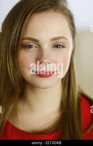 Kopfaufnahme einer intelligenten, selbstbewussten, lächelnden, tausendjährigen europäischen Frau, die zu Hause mit gefalteten Armen steht. Attraktive junge Teenager Student Mädchen Freiberufler Stockfoto