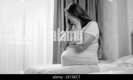 Schwarz-weiß-Bild von jungen schwangeren Frau leiden an Depressionen weinen auf dem Bett. Konzept der mütterlichen und Schwangerschaftsdepression Stockfoto