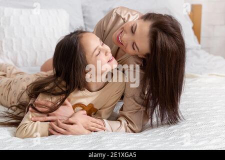 Liebe zwischen Eltern und Kind. Fröhliche junge Frau umarmt ihre niedliche Teenager-Tochter auf dem Bett zu Hause Stockfoto