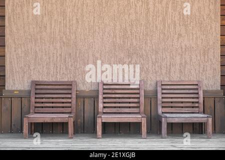 Drei leere Holzstühle zum Entspannen auf der Außenterrasse des Hotels. Holzverkleidung. Grafische symmetrische Linien. Speicherplatz kopieren. Stockfoto