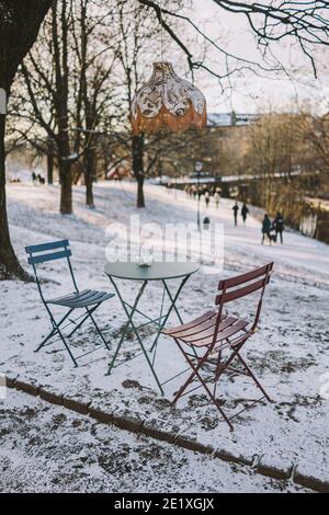 Outdoor-Café mit Stühlen und Lampe über Metalltisch mit den Menschen, die im Hintergrund zu Fuß in Sagene in Oslo, Norwegen im Winter und Schnee Stockfoto