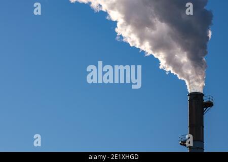 Dicker Rauch weht in einen klaren blauen Himmel von der Spitze eines hohen Schornstein. Stockfoto