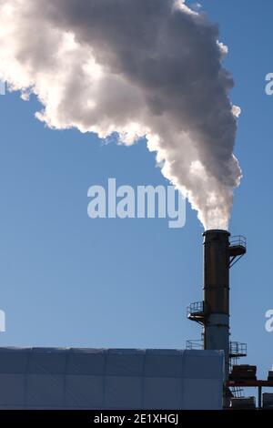 Dicker Rauch weht in einem vertikal ausgerichteten Bild von einem hohen Rauchschwamm in einen blauen Himmel. Stockfoto