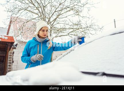 Frau kratzt Eis von der Frontscheibe ihres Autos Im Winter Stockfoto