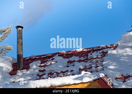 Rauch aus dem Kamin auf dem schneebedeckten Dach des Hauses Stockfoto