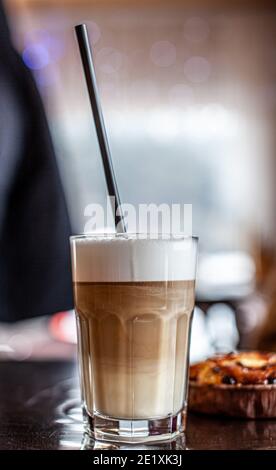 Heißer Latte-Kaffee in einem Glas und ein frischer Apfel-Dessert daneben. Das heiße Getränk wird mit einem Plastikstroh serviert. Leckeres Frühstück im Café Stockfoto