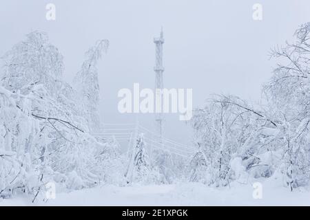 Vereisten Zellenturm und elektrische Drähte zwischen einem verschneiten Wald Auf einem Berg gegen einen Winterhimmel Stockfoto