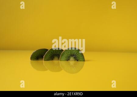 Drei Scheiben Kiwi Hälften liegen in einer Reihe auf Trend iluminaited gelb mit einer Kopie der Platz für Text. Stockfoto