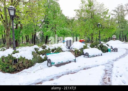 Bänke und Gehweg von Schnee im Park bedeckt. Unerwarteter Schneesturm in der Stadt Stockfoto