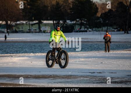 Radfahren im Winter. Mann trägt grüne Jacke Reiten Fett Fahrrad auf Hietaranta Strand im Winter. Helsinki, Finnland. Stockfoto