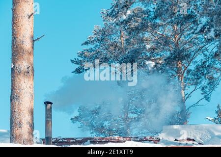 Rauch aus dem Kamin auf dem schneebedeckten Dach des Hauses Stockfoto