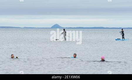Portobello, Schottland, Großbritannien. 10. Januar 2021. Trotz einer derzeit in Schottland erzwungenen nationalen Sperre waren Portobello Promenade und Strand mit einer großen Anzahl von Menschen beschäftigt, die dort am Sonntagnachmittag waren. Mehrere Polizeipatrouillen waren offensichtlich, dass sie meist unauffällig blieben, aber die Beamten sprachen mit den Kaffeehäffern, um sie zu drängen, die soziale Distanz zwischen den Kunden korrekt zu halten. PIC; Open Water Schwimmer und Paddelboarder . Iain Masterton/Alamy Live News Stockfoto