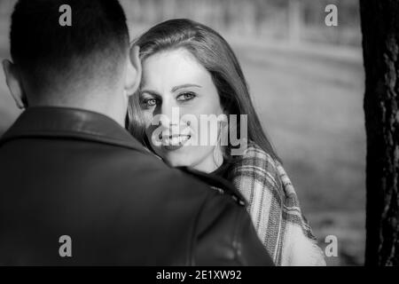 Junge Frau steht neben Freund mit einem Lächeln, während sie zur Seite schaut. Schwarzweiß-Fotografie. Valentinstag, Dating-Konzepte Stockfoto