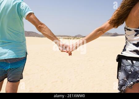 Einsames Paar mit Händen auf leeren Sanddünen im Corralejo Naturpark zu Fuß. Junge Männer und Frauen erkunden Wüste an sonnigen Tagen auf Fuerteventura Stockfoto