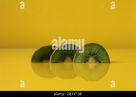 Drei Scheiben Kiwi Hälften liegen in einer Reihe auf Trend iluminaited gelb mit einer Kopie der Platz für Text. Stockfoto