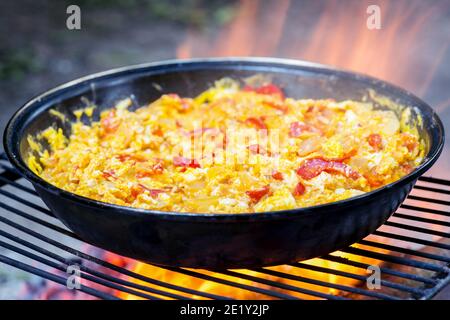Omelette mit Gemüse in einer Pfanne auf dem Grill close-up in der feurigen Flamme des Feuers. Das Konzept der Leichtigkeit des Kochens in der Natur. Selektiver Fokus Stockfoto