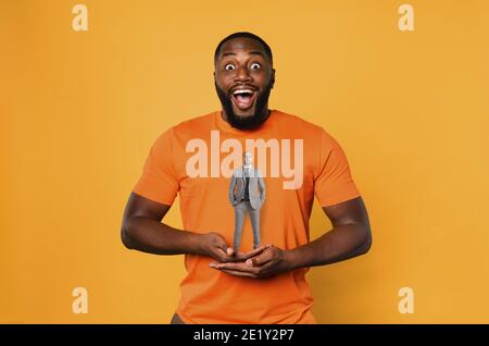 Glücklicher Afro Mann hält einen Geschäftsmann mit Händen. Orangefarbener Hintergrund Stockfoto