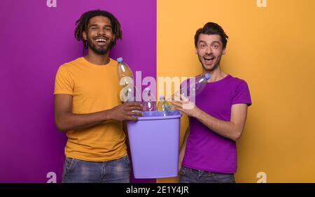 Freunde halten ein Kunststoffbehälter mit Flaschen über Gelb und Violett. Konzept der Ökologie, Umweltschutz, Recycling und Nachhaltigkeit Stockfoto