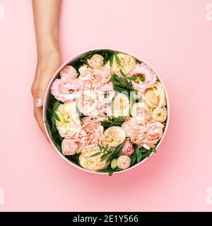 Florist hält einen Hut runde Box mit floralen Komposition auf einem rosa Hintergrund mit Copy Space. Geschenkbox für 8. März, Valentinstag, Muttertag Stockfoto