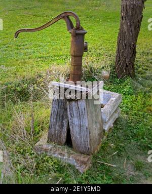 Alte rostige Handpumpe auf einem verfaulten Holzsockel auf einer Wiese, Österreich Stockfoto