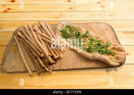 Brotscheiben und zerkleinerte Focaccia mit Öl mit Rucola Blätter Auf Holzschneidebrett Stockfoto