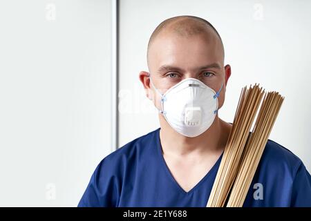 Erfahrene männliche Masseur Masseur in seinem medizinischen Büro tragen professionelle Uniform und Einweg-Atemschutzmaske Gesichtsmaske. Hält traditionelle Stockfoto