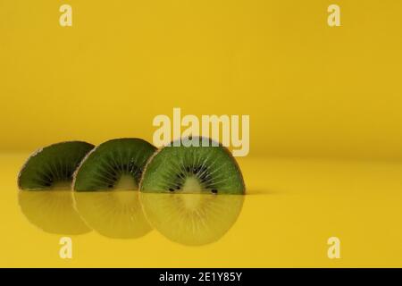 Drei Scheiben Kiwi Hälften liegen in einer Reihe auf Trend iluminaited gelb mit einer Kopie der Platz für Text. Stockfoto