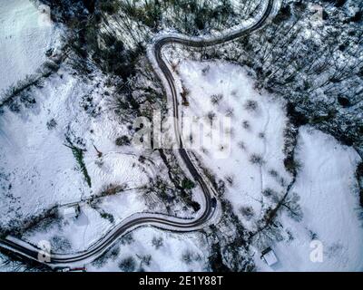 Luftaufnahme einer kurvenreichen Straße durch verschneite Landschaft in den Bergen von Asturien in Spanien. Winterzeit. Stockfoto