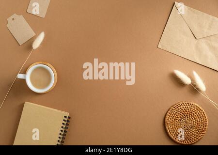 Eleganter femininer Arbeitsplatz mit Tasse Kaffee, Papierumschlag, Notizbuch, trockenen Blumen auf braunem Hintergrund. Vintage Home Office Schreibtisch, Ansicht von oben. Stockfoto