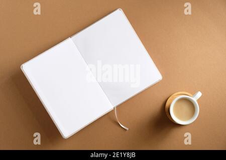 Leeres Buch und eine Tasse Kaffee auf braunem Hintergrund geöffnet. Flach liegend, Draufsicht. Gemütlicher Schreibtisch für zu Hause. Stockfoto