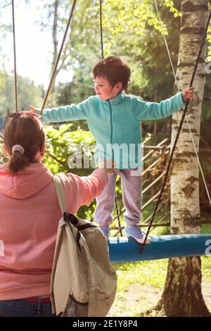 Familie im Vergnügungspark. Mama hilft dem Kind auf dem Hindernisparcours zu bleiben Stockfoto