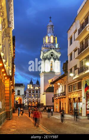 Nachtszene entlang der Garcia Moreno Straße in Quito, Ecuador mit dem Turm der Kathedrale von Quito, der über der Szene ragt. Stockfoto