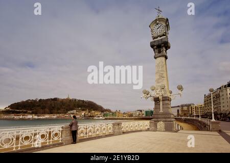 2020 02, San Sebastian, Spanien. Frau vor dem Meer von Donostia mit dem Rathaus und dem Schloss Mota im Hintergrund. Stockfoto