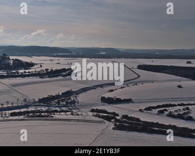 Luftaufnahme der Niedergebirge Schwäbische Alb in der Wintersaison mit schneebedeckten Landschaft von Feldern und Wäldern mit Parkplatz und Landstraße. Stockfoto