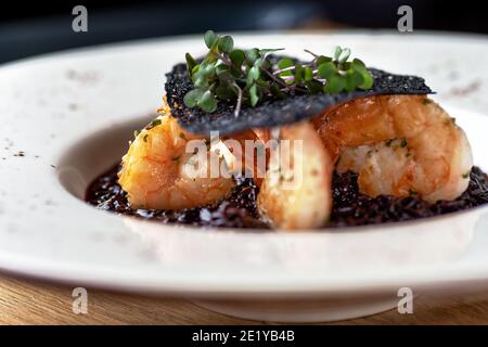 Risotto mit schwarzem Reis. Garnelen Risotto auf einem weißen Teller auf dem Tisch, serviert in einem Restaurant, Menü Food-Konzept. Stockfoto