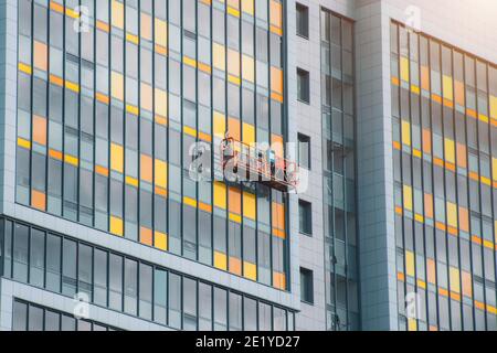 Ein Konstruktionsteam in einer aufgehängten Halterung an Kabeln ist Arbeiten an der Fassade des Gebäudes Stockfoto