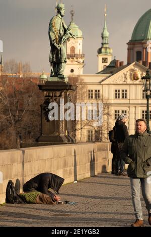 Prag, Tschechische Republik. 01-09-2021. Bettler, der auf der Karlsbrücke Geld verlangt, bei einem Sonnenuntergang im Winter in Prag. Stockfoto
