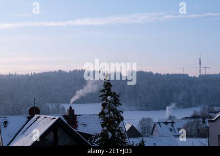 Blick über schneebedeckte Dächer mit rauchenden Kaminen in einem Dorf bei Sonnenaufgang Stockfoto