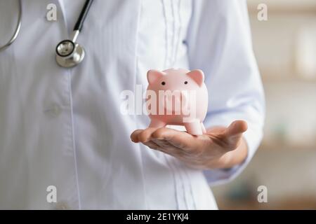 Junge Hausärztin mit Sparschwein in den Händen. Stockfoto