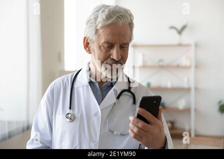 Älterer Arzt im mittleren Alter mit Smartphone-Apps. Stockfoto