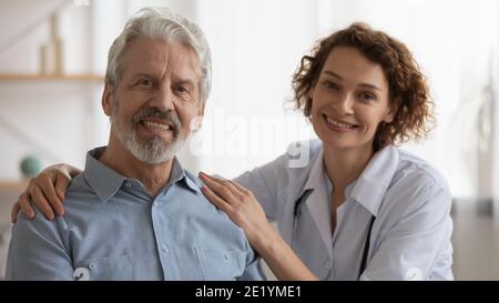 Portrait von lächelnd freundlich Krankenschwester umarmt Schultern des alten Mannes. Stockfoto