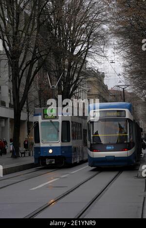 Zwei Straßenbahnen in blauer Farbe, die sich in entgegengesetzter Richtung im Stadtzentrum von Zürich, an der Bahnhofstraße, der berühmten und teuren Straße, vorbeiziehen. Stockfoto