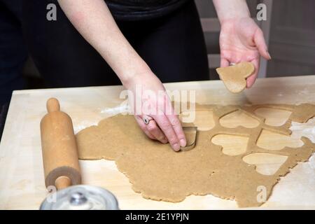 Weibliche Hände bereiten hausgemachte Kekse in Form eines Herzens zu. Horizontal. Stockfoto