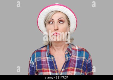 Closeup Portrait von Crazy crosseyed stilvolle reife Frau im lässigen Stil mit weißen Hut stehend, gekreuzte Augen und suchen mit lustigen Gesichtsausdruck. Stockfoto