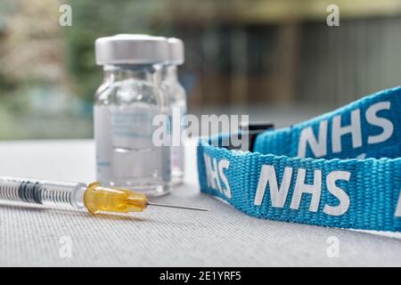 Stafford, Vereinigtes Königreich - Januar 10 2021: NHS-Impfstoff-Konzept. Spritze, Injektionsfläschchen und NHS-Trageschlaufe. Selektiver Fokus. Stockfoto