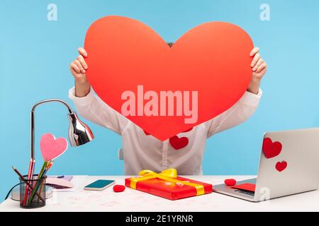 Männliche Büroangestellte versteckt, hält in den Händen großen roten Papier Herz, Vorbereitung Dekoration und Geschenk für st. valentinstag Feier. Innenaufnahme im Studio Stockfoto