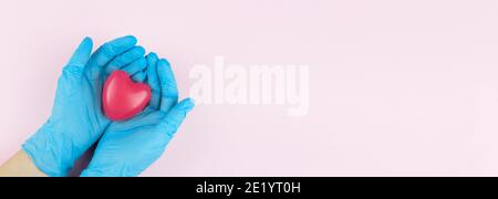 Ärztehand mit blauen medizinischen Handschuhen mit rotem Herz, medizinisches Versicherungskonzept. Symbol des Herzens in den Händen eines Arztes auf rosa Hintergrund Stockfoto