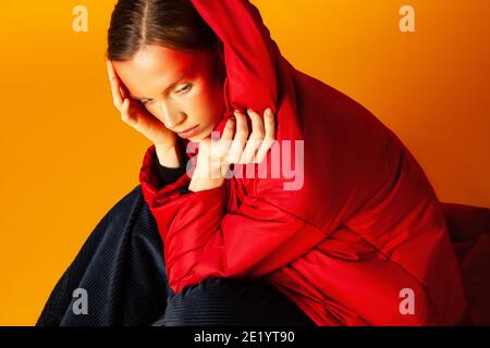 Einsame Frau, die in einen baggy Mantel vor gelbem Hintergrund einwickelt Stockfoto